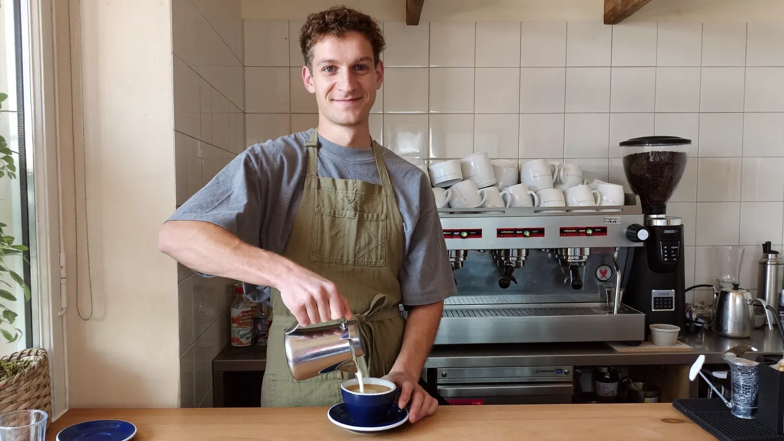 Jun behind the counter pouring milk into a blue enamel cup